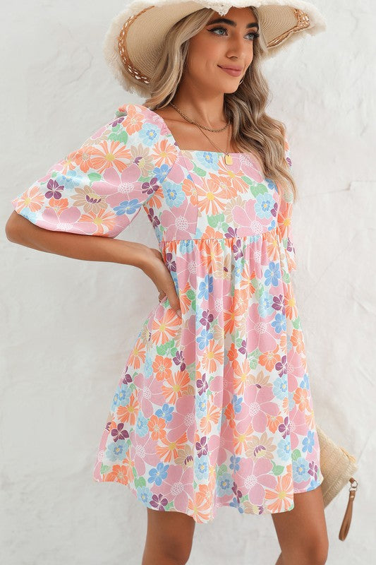 The Square Neck Bubble Puff Sleeve Floral Coral Dress, featuring a vibrant floral design on a light pink background, is elegantly displayed on a hanger against a plain white wall.