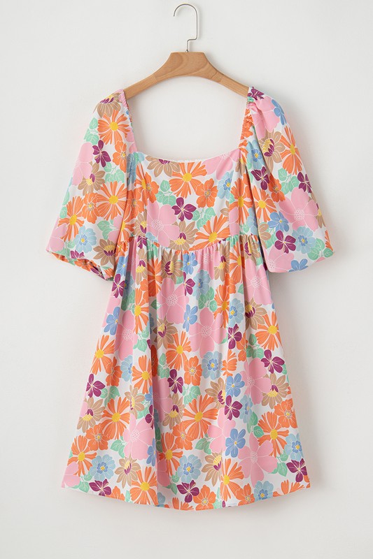 The Square Neck Bubble Puff Sleeve Floral Coral Dress, featuring a vibrant floral design on a light pink background, is elegantly displayed on a hanger against a plain white wall.