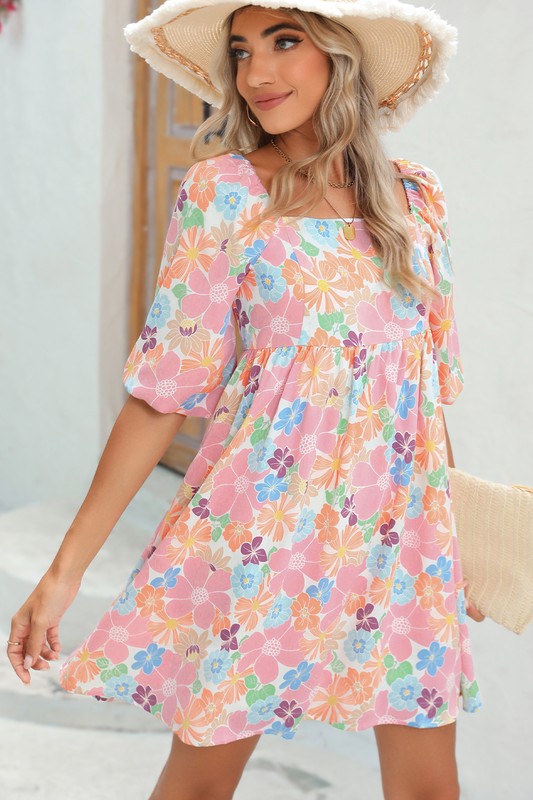 The Square Neck Bubble Puff Sleeve Floral Coral Dress, featuring a vibrant floral design on a light pink background, is elegantly displayed on a hanger against a plain white wall.