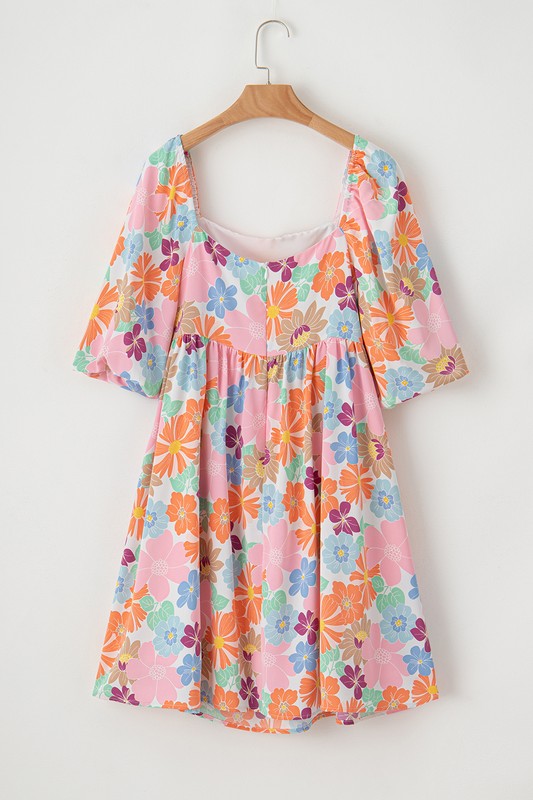 The Square Neck Bubble Puff Sleeve Floral Coral Dress, featuring a vibrant floral design on a light pink background, is elegantly displayed on a hanger against a plain white wall.