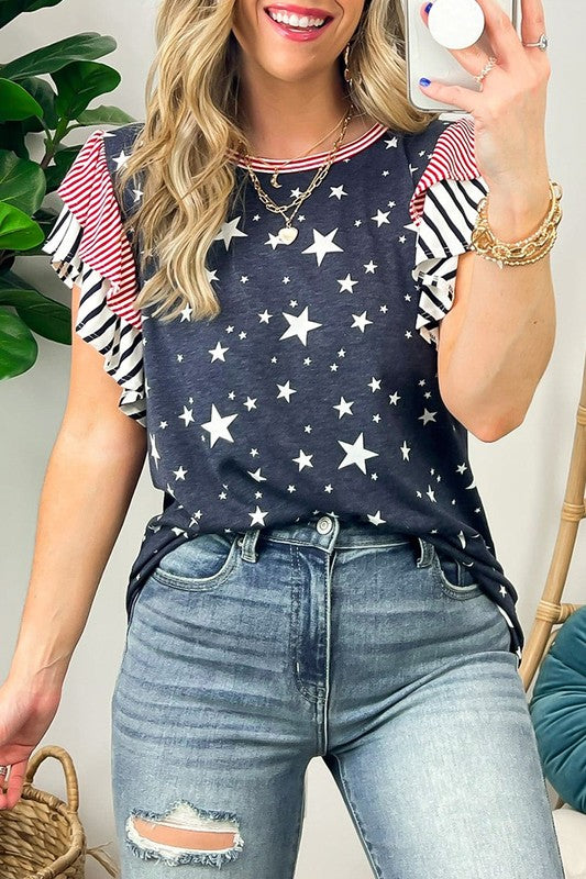 A woman displays American pride in the Flag Stripe Ruffle Sleeve Star Shirt USA, featuring a star pattern and striped ruffled sleeves, paired with denim shorts. Her look is accentuated with bracelets and a necklace, all crafted from soft cotton fabric for added comfort and style.