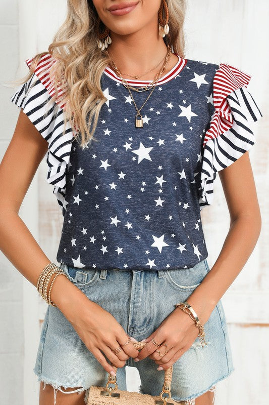 A woman displays American pride in the Flag Stripe Ruffle Sleeve Star Shirt USA, featuring a star pattern and striped ruffled sleeves, paired with denim shorts. Her look is accentuated with bracelets and a necklace, all crafted from soft cotton fabric for added comfort and style.