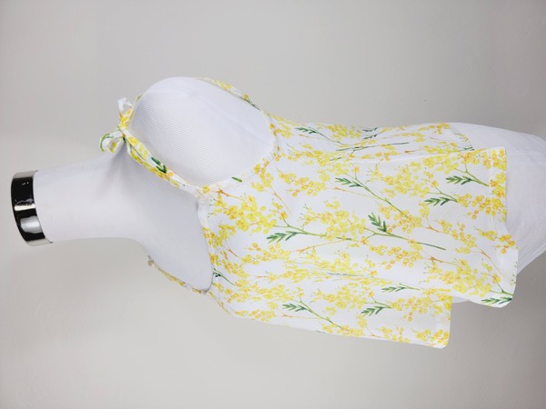 Yellow cotton tank top with a floral design and adjustable spaghetti straps, styled against a leafy green plant on a white background.