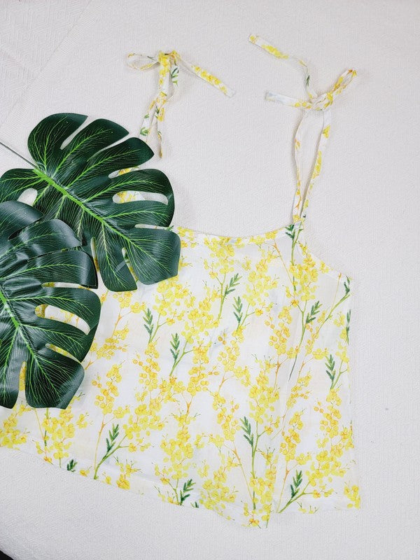 Yellow cotton tank top with a floral design and adjustable spaghetti straps, styled against a leafy green plant on a white background.