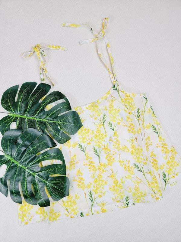 Yellow cotton tank top with a floral design and adjustable spaghetti straps, styled against a leafy green plant on a white background.