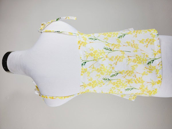 Yellow cotton tank top with a floral design and adjustable spaghetti straps, styled against a leafy green plant on a white background.