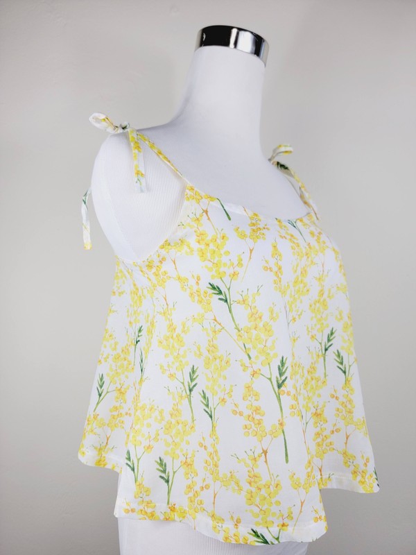 Yellow cotton tank top with a floral design and adjustable spaghetti straps, styled against a leafy green plant on a white background.