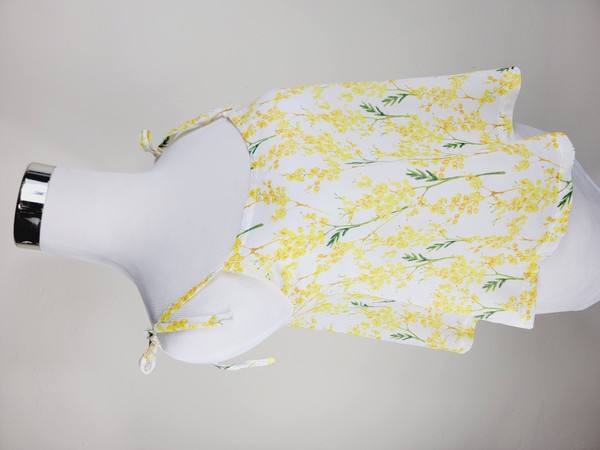 Yellow cotton tank top with a floral design and adjustable spaghetti straps, styled against a leafy green plant on a white background.