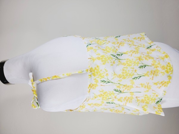 Yellow cotton tank top with a floral design and adjustable spaghetti straps, styled against a leafy green plant on a white background.