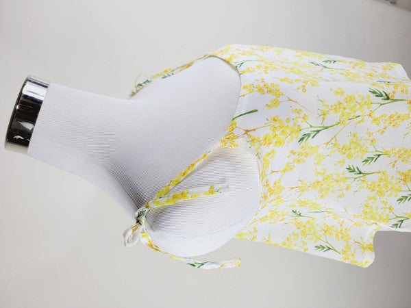 Yellow cotton tank top with a floral design and adjustable spaghetti straps, styled against a leafy green plant on a white background.