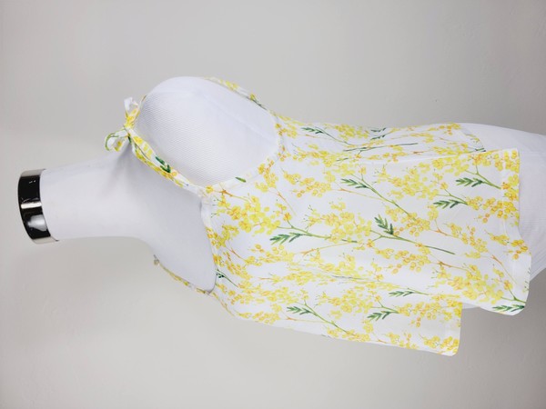 Yellow cotton tank top with a floral design and adjustable spaghetti straps, styled against a leafy green plant on a white background.