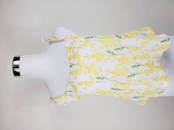 Yellow cotton tank top with a floral design and adjustable spaghetti straps, styled against a leafy green plant on a white background.