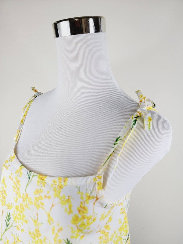 Yellow cotton tank top with a floral design and adjustable spaghetti straps, styled against a leafy green plant on a white background.