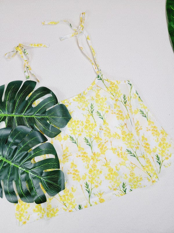 Yellow cotton tank top with a floral design and adjustable spaghetti straps, styled against a leafy green plant on a white background.