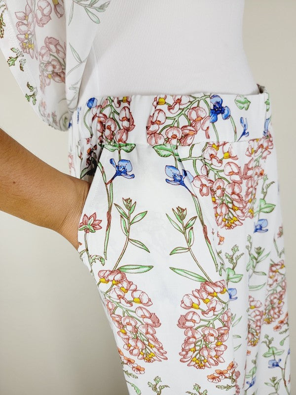 White pants with a vibrant floral pattern showcasing shades of blue, green, red, and pink. Made from airy cotton fabric, these wide-leg pants come with an elastic waistband for ultimate comfort.