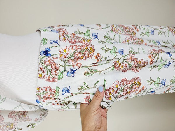 White pants with a vibrant floral pattern showcasing shades of blue, green, red, and pink. Made from airy cotton fabric, these wide-leg pants come with an elastic waistband for ultimate comfort.