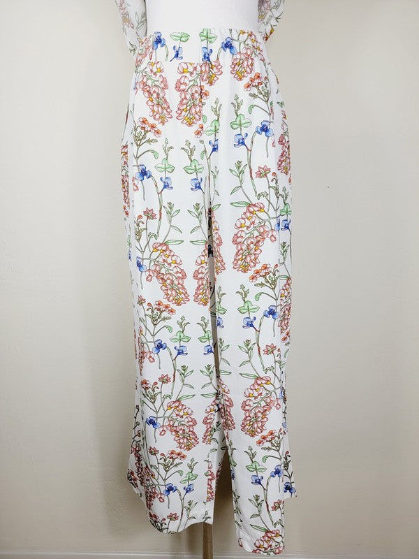 White pants with a vibrant floral pattern showcasing shades of blue, green, red, and pink. Made from airy cotton fabric, these wide-leg pants come with an elastic waistband for ultimate comfort.