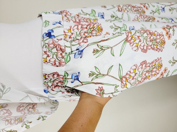 White pants with a vibrant floral pattern showcasing shades of blue, green, red, and pink. Made from airy cotton fabric, these wide-leg pants come with an elastic waistband for ultimate comfort.