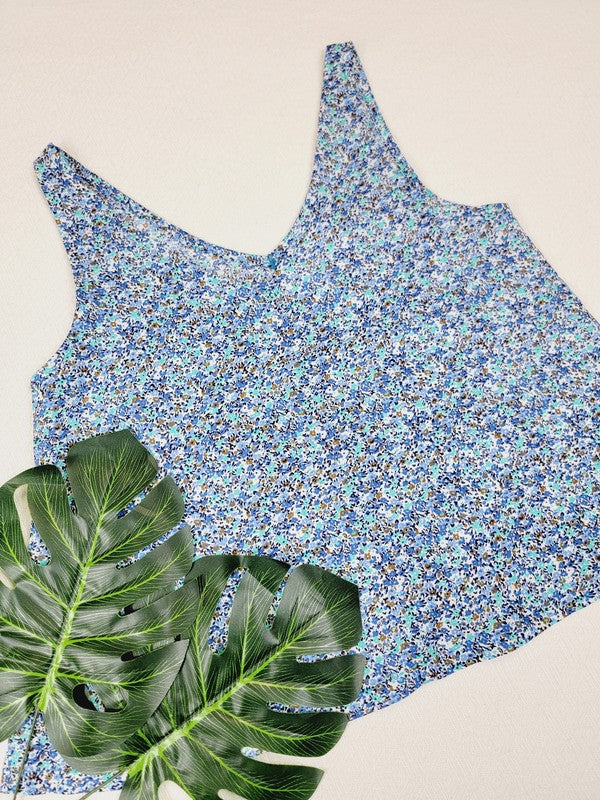 A Cotton Tank Top, designed in a boho style with adjustable straps and crafted from luxurious Turkish cotton, is laid flat on a light surface with two green monstera leaves placed nearby.