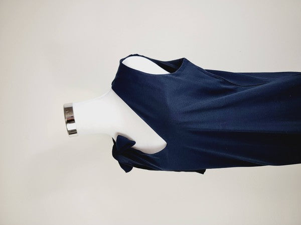 A mannequin displays a Cotton Jersey dress in navy blue with side pockets, featuring a sleeveless design and a large bow on the left shoulder.