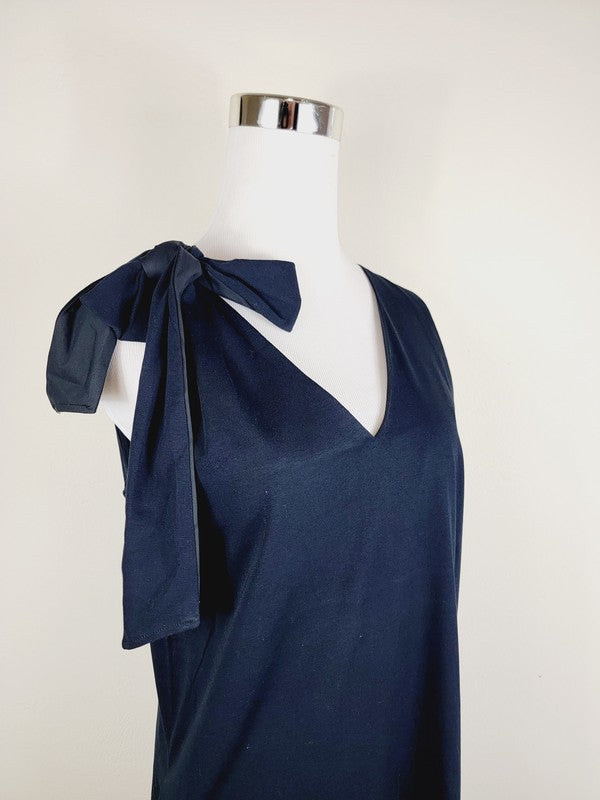 A Cotton Jersey dress in dark grey Turkish cotton, displayed on a mannequin, featuring an adjustable tie shoulder with a large bow on the left side and pockets, set against a plain white background.