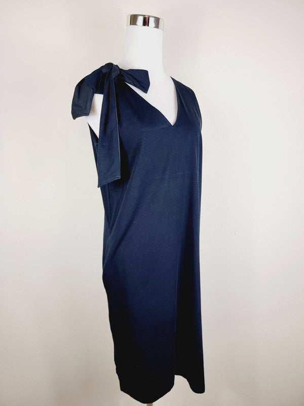 A Cotton Jersey dress in dark grey Turkish cotton, displayed on a mannequin, featuring an adjustable tie shoulder with a large bow on the left side and pockets, set against a plain white background.