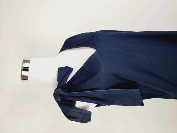 A mannequin displays a Cotton Jersey dress in navy blue with side pockets, featuring a sleeveless design and a large bow on the left shoulder.