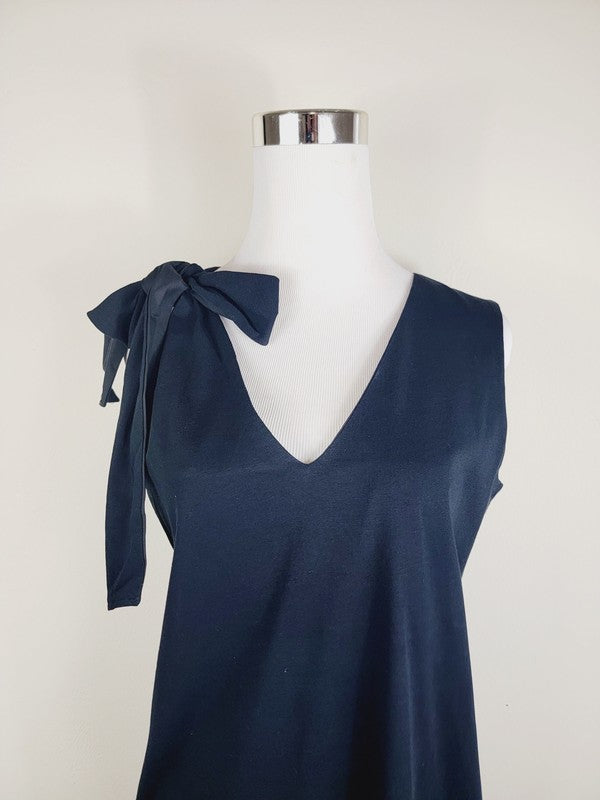 A Cotton Jersey dress in dark grey Turkish cotton, displayed on a mannequin, featuring an adjustable tie shoulder with a large bow on the left side and pockets, set against a plain white background.