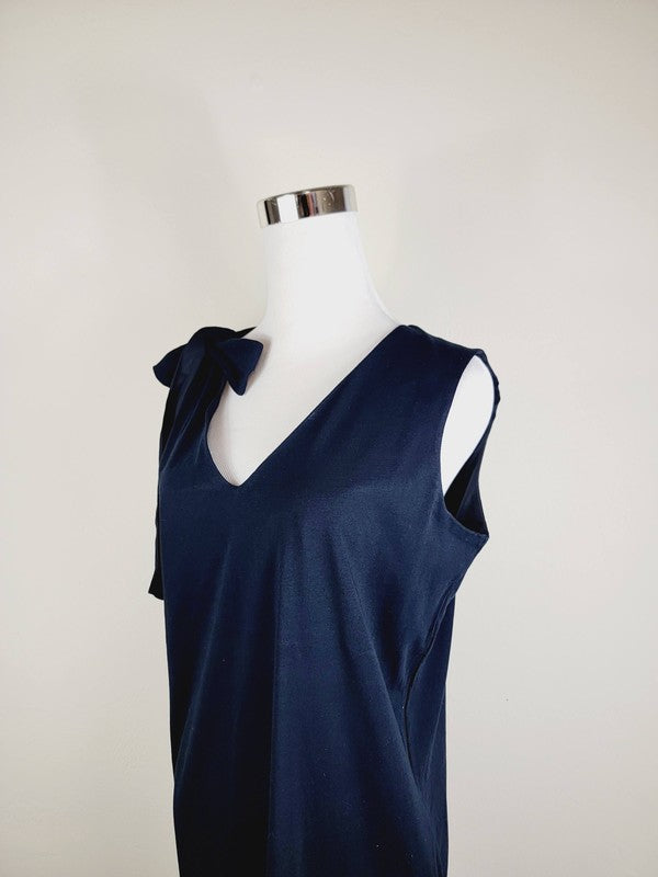 A mannequin displays a Cotton Jersey dress in navy blue with side pockets, featuring a sleeveless design and a large bow on the left shoulder.