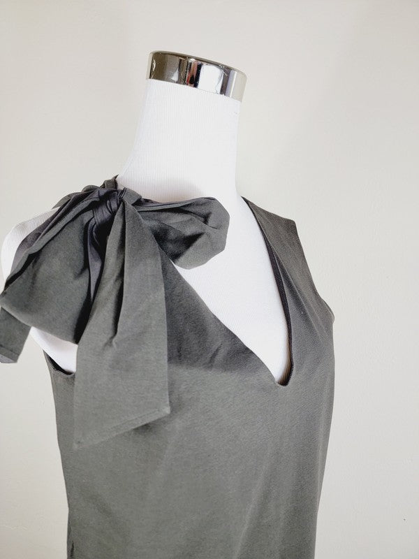 A Cotton Jersey dress in dark grey Turkish cotton, displayed on a mannequin, featuring an adjustable tie shoulder with a large bow on the left side and pockets, set against a plain white background.