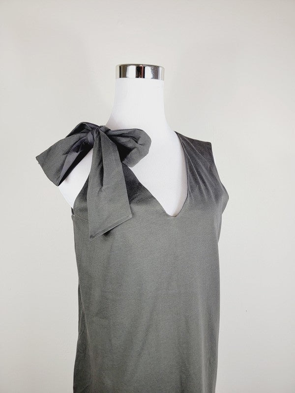 A Cotton Jersey dress in dark grey Turkish cotton, displayed on a mannequin, featuring an adjustable tie shoulder with a large bow on the left side and pockets, set against a plain white background.