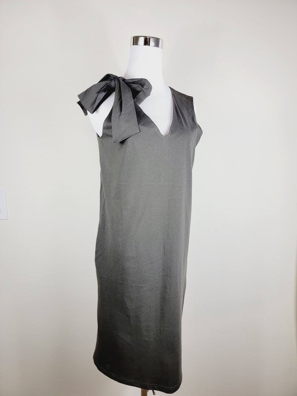 A Cotton Jersey dress in dark grey Turkish cotton, displayed on a mannequin, featuring an adjustable tie shoulder with a large bow on the left side and pockets, set against a plain white background.