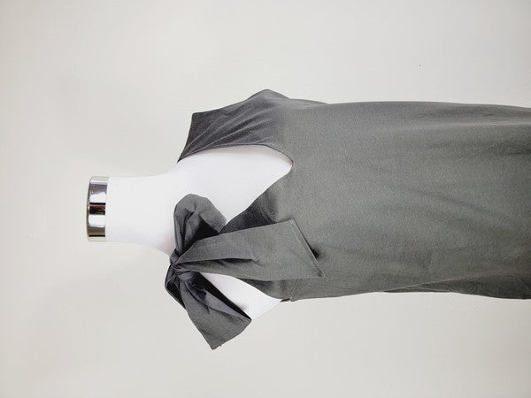 A Cotton Jersey dress in dark grey Turkish cotton, displayed on a mannequin, featuring an adjustable tie shoulder with a large bow on the left side and pockets, set against a plain white background.