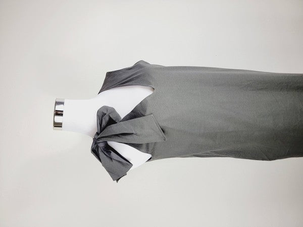 A Cotton Jersey dress in dark grey Turkish cotton, displayed on a mannequin, featuring an adjustable tie shoulder with a large bow on the left side and pockets, set against a plain white background.