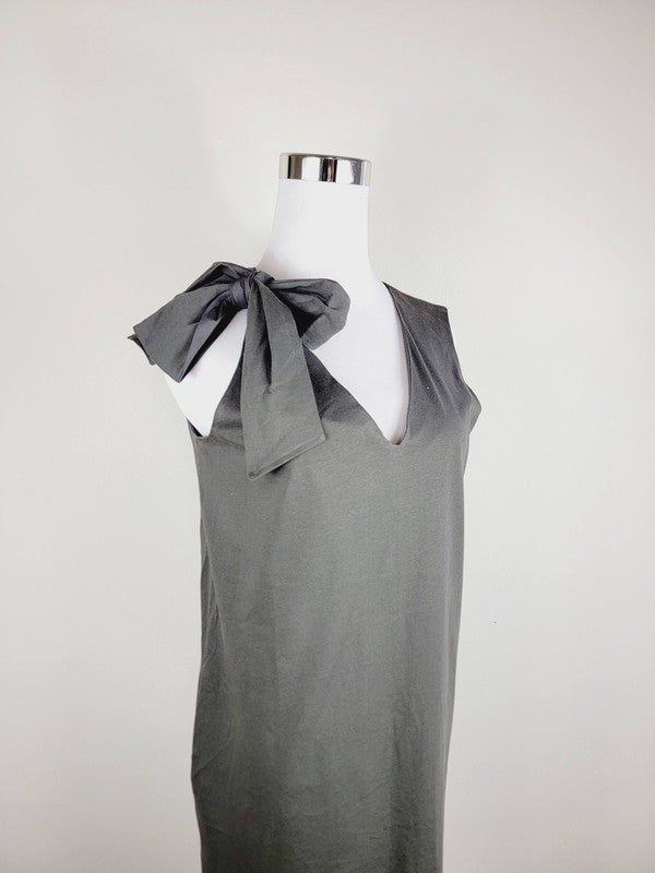 A Cotton Jersey dress in dark grey Turkish cotton, displayed on a mannequin, featuring an adjustable tie shoulder with a large bow on the left side and pockets, set against a plain white background.