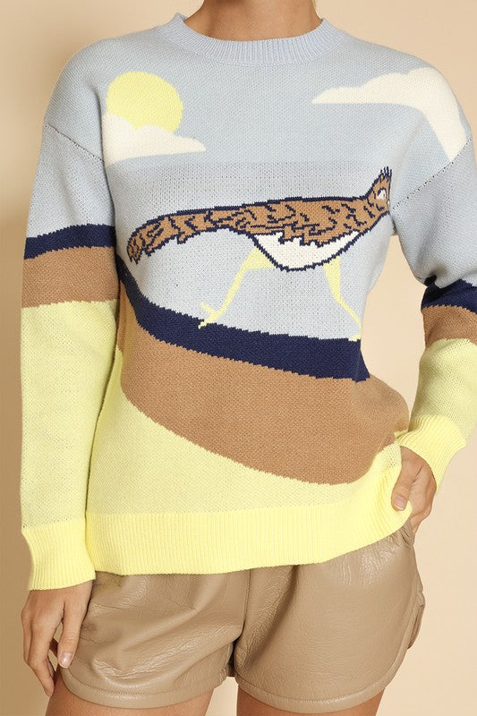 A woman stands against a beige background, wearing the Roadrunner knit sweater, featuring an exclusive in-house road runner intarsia design, and beige shorts.