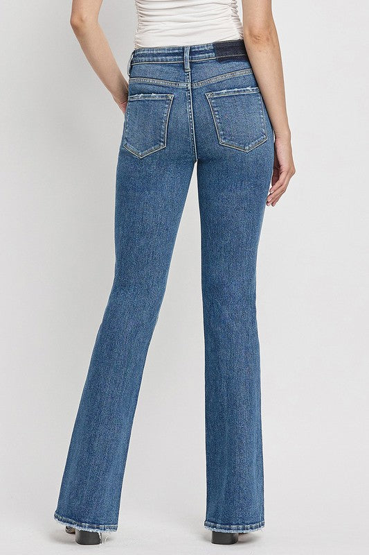 A person is wearing the High Rise Slant Hem Flare Jeans crafted from stretch denim, matched with black sandals, and standing against a plain white backdrop. The jeans' flattering fit enhances a chic and contemporary look.