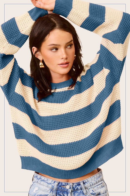 A person wearing a Striped Round Neck Loose Fit Sweater in pink and white with arms raised, paired with loose fit blue jeans.