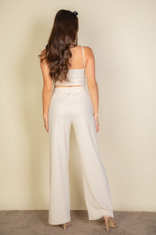 Sporting the Bustier Cami Top & Slant Straight Pants, a person poses against a light-colored background, accessorized with sunglasses and open-toed shoes.