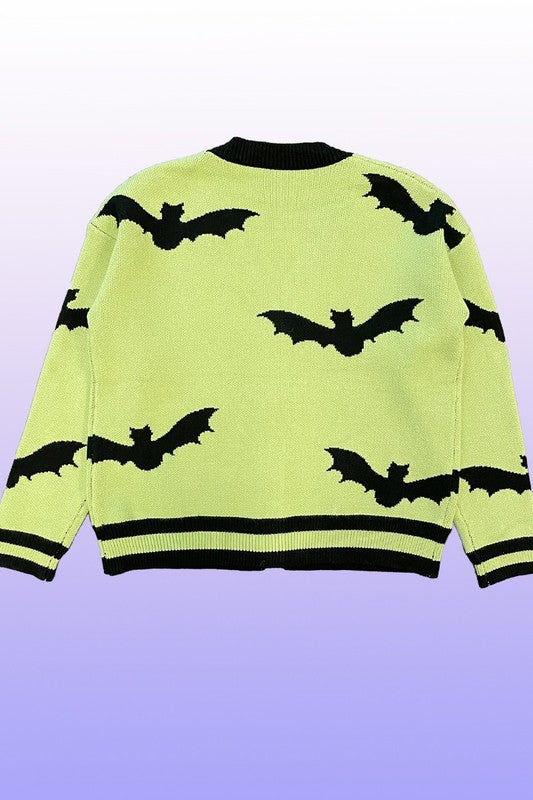 An exclusive in-house design, the PLUS SIZE Halloween knit cardigan features black bat intarsia patterns, black trim, and a black button closure on a lime green background. Set against a gradient backdrop transitioning from light purple at the top to blue at the bottom, this piece offers added comfort and style for plus sizes.