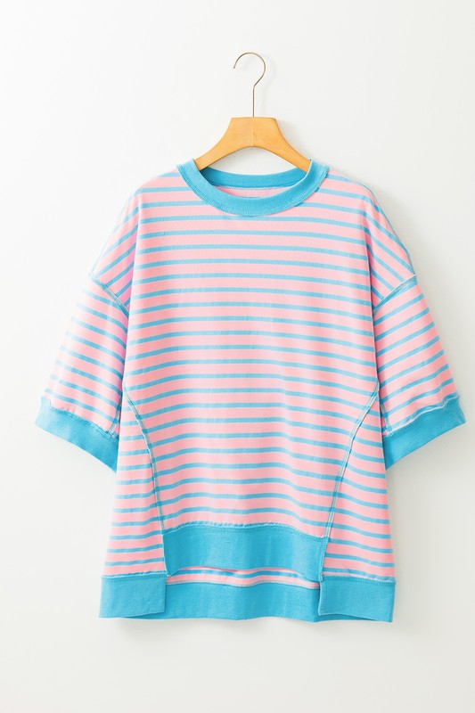 The Pink Mint Stripe Color Block Oversized T Shirt Top, featuring a relaxed short-sleeve design with pink and blue stripes, hangs stylishly on a wooden hanger against a white backdrop.