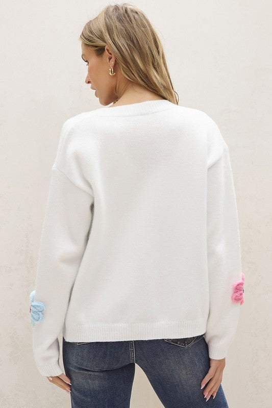 A woman, wearing the Cute Flower Pattern Button-Up Cardigan in pink with floral embroidery crafted from cozy rib-knit fabric, paired with a white top and blue jeans, smiles as she touches her hair.