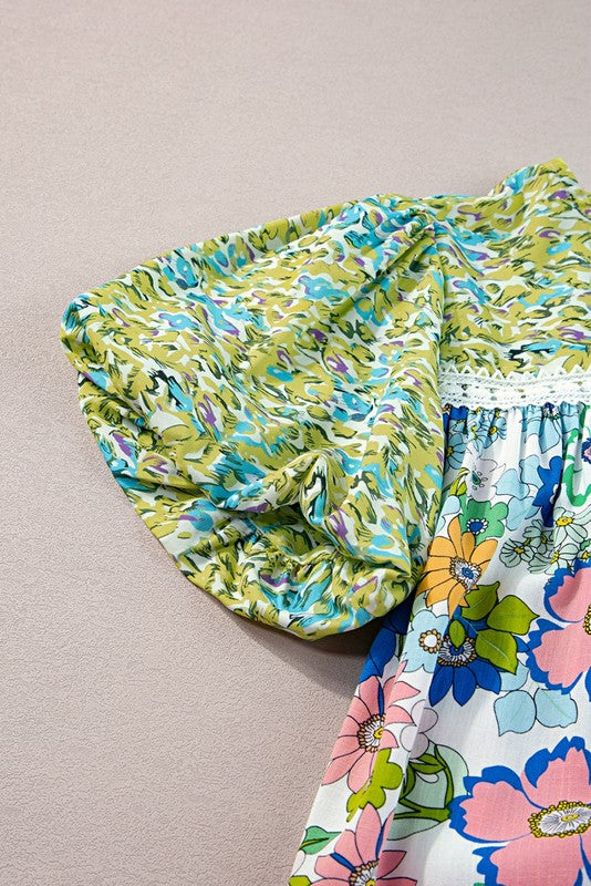 A short-sleeved tunic with bubble sleeves, featuring a lace panel on the chest and a retro pattern of green, blue, pink, and orange flowers on a white background.
