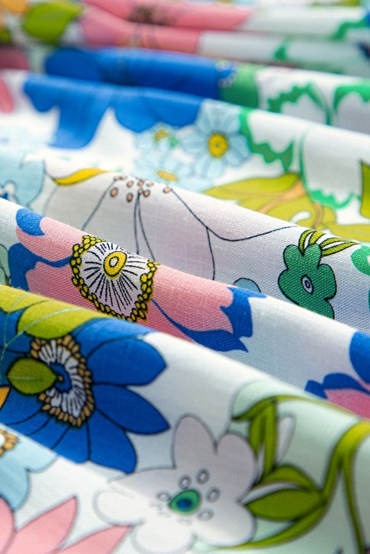 A short-sleeved tunic with bubble sleeves, featuring a lace panel on the chest and a retro pattern of green, blue, pink, and orange flowers on a white background.