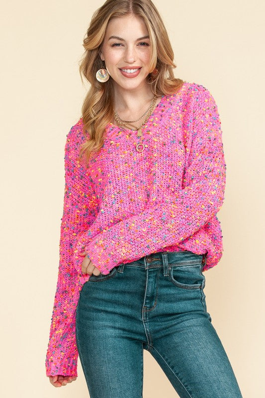 A person with long hair is wearing a Mixed Color Chunky Knit Sweater, blue jeans, and jewelry, standing against a plain background.