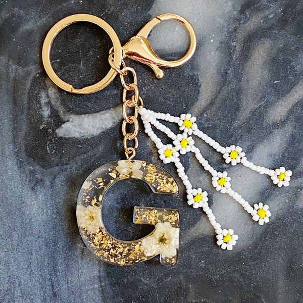 Baby Daisy Initial Key Chain alphabet keychains with real daisy flowers and gold flakes on a marble surface.