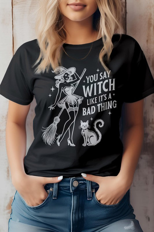 A person shows off the "You Say Witch Like It's a Bad Thing" Graphic Tee, an eco-friendly shirt adorned with a witch, her broom, and a cat. Ideal for Halloween or anytime you want to embrace your inner magic with sustainable style.