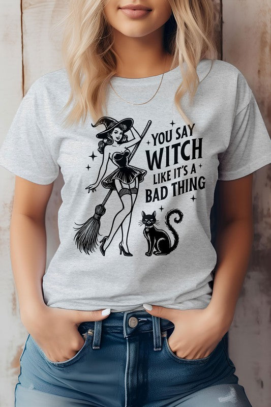 A person shows off the "You Say Witch Like It's a Bad Thing" Graphic Tee, an eco-friendly shirt adorned with a witch, her broom, and a cat. Ideal for Halloween or anytime you want to embrace your inner magic with sustainable style.