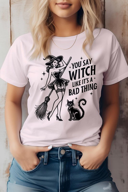 A person shows off the "You Say Witch Like It's a Bad Thing" Graphic Tee, an eco-friendly shirt adorned with a witch, her broom, and a cat. Ideal for Halloween or anytime you want to embrace your inner magic with sustainable style.