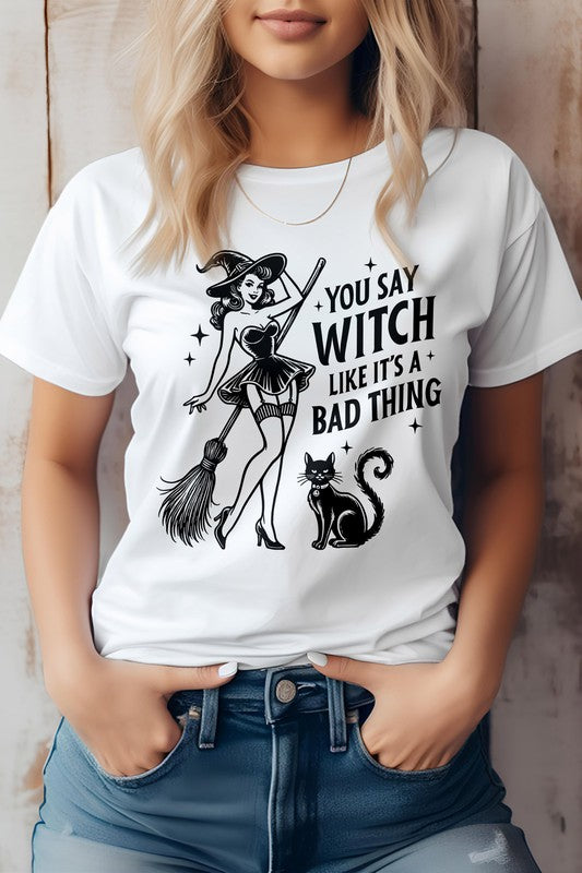 A person shows off the "You Say Witch Like It's a Bad Thing" Graphic Tee, an eco-friendly shirt adorned with a witch, her broom, and a cat. Ideal for Halloween or anytime you want to embrace your inner magic with sustainable style.